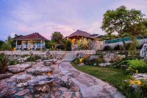 a house with a stone wall and a garden at Bukit Taman Cottages in Nusa Lembongan