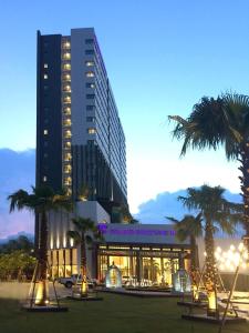 a large building with palm trees in front of it at Grand Fortune Hotel Nakhon Si Thammarat in Nakhon Si Thammarat