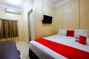 1 dormitorio con 1 cama con almohadas rojas y TV en RedDoorz @ Jalan Setiabudi Semarang en Semarang