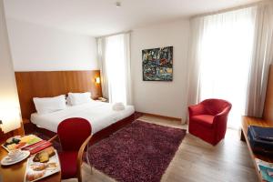 ヴィチェンツァにあるヴィチェンツァ ティエポロ ホテルのベッドと赤い椅子が備わるホテルルームです。