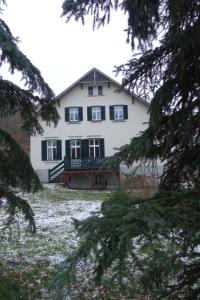 ein weißes Haus mit schwarzen Fenstern und Bäumen in der Unterkunft Pension Gräfliche Villa in Reitwein
