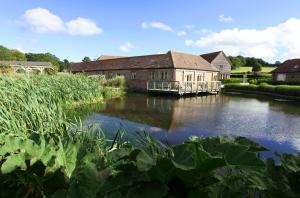 a building next to a river with plants in the foreground at Whytings Stud Barn 1 in Horsham