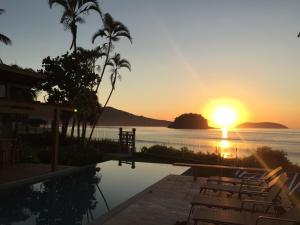a sunset over the water with chairs and a pool at Villa Sapê Pousada in Ubatuba
