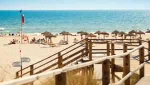 ein Strand mit Sonnenschirmen und Menschen auf dem Sand in der Unterkunft Apartamentos Dom Henrique in Monte Gordo