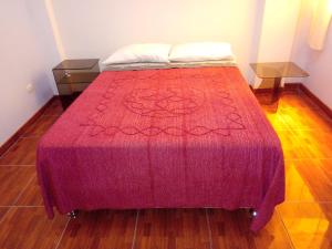a bed with a red blanket and two tables at Hostal Sotillo in Ilo