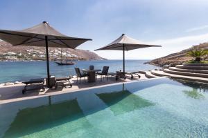 a pool with chairs and umbrellas next to the ocean at Kivotos Mykonos in Ornos