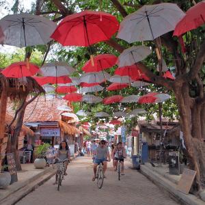 people riding bikes down a street with red and white umbrellas at Koi Gili Guest House in Gili Trawangan