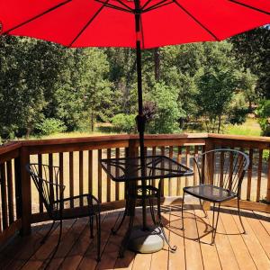 a table and chairs on a deck with a red umbrella at Queen's Inn By The River in Oakhurst