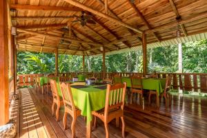 un restaurante con mesas verdes y sillas en una terraza de madera en La Cusinga Lodge, en Uvita