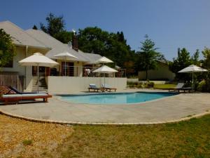 a swimming pool with chairs and umbrellas next to a house at Lauradale Accommodation in Stellenbosch