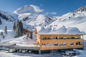 una casa en la nieve con una montaña en el fondo en Wolfegg Appartement - Cafe - Bistro en Warth am Arlberg