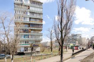 a tall building next to a park with trees at ARTAL Apartment Yordanska Street 22 in Kyiv
