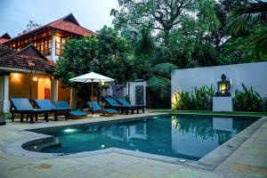 Una piscina con sillas y una sombrilla al lado de una casa. en Flamingo Boutique Hotel & Ayurvedic spa, en Mararikulam