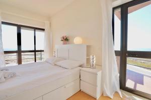 - une chambre blanche avec un lit et de grandes fenêtres dans l'établissement Deluxe Oceanfront - Vue Sur la Mer, à Peniche