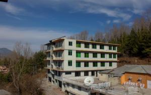 un grand bâtiment blanc avec des fenêtres vertes à côté des arbres dans l'établissement Green Valley Bhurban Apartments, à Bhurban