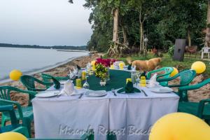 una mesa en la playa con un perro de pie alrededor en Mirembe Resort Beach Hotel Ssese en Kalangala