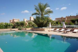 a swimming pool with chairs and umbrellas and a palm tree at Palais Villa Talaa Resort in Taroudant