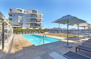a swimming pool with an umbrella and chairs and a building at Waterfront Stays in Cape Town