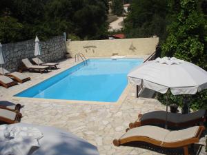 a swimming pool with chairs and an umbrella at Kiki Apartments in Fiskardo