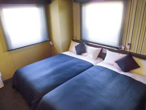 two twin beds in a room with two windows at HOTEL LiVEMAX Fukuyama Ekimae in Fukuyama