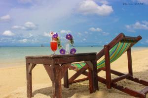 a table on the beach with a chair and a drink at Phi Phi Relax Beach Resort in Phi Phi Islands