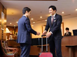 dos hombres de traje estrechando la mano con una maleta en Ark Hotel Kumamotojo Mae -ROUTE INN HOTELS-, en Kumamoto