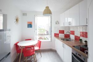 a white kitchen with red chairs and a white table at Tout à pied - Appartement - parking privé - 80m des falaises - Plein centre in Étretat