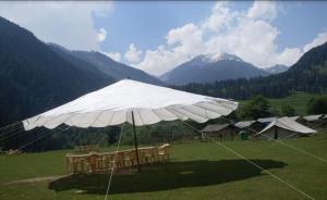 a large white umbrella with chairs and tents in a field at Aru Camping Resort Aru, J&K in Pahalgām