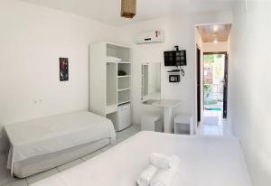a white bedroom with two beds and a television at Pousada Brasil Caribe in Morro de São Paulo