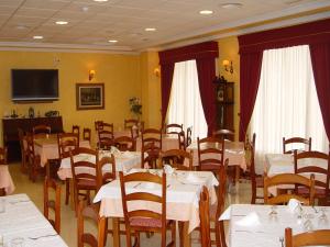 un restaurant avec des tables et des chaises blanches et une télévision dans l'établissement Hotel Albohera, à Santiago de la Ribera