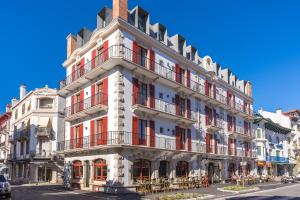 a tall white building with red balconies on a street at Hôtel & Spa Madison Saint Jean de Luz in Saint-Jean-de-Luz