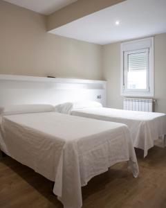 two beds with white sheets in a white room at Casa Canosa in A Coruña