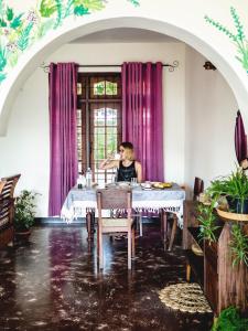 una donna seduta a un tavolo in una stanza con tende viola di Holiday Stay Inn a Kandy