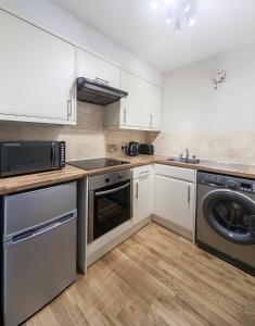 cocina con armarios blancos, lavadora y secadora en Ardconnel Apartment, en Inverness