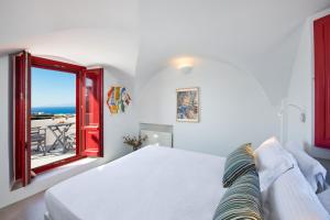 a white bedroom with a bed and a window at Aplada Suites in Oia