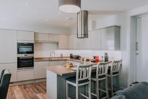 a kitchen with white cabinets and a island with bar stools at Cavendish House with Secure, Allocated Parking, 2 mins walk from Windsor Castle in Windsor
