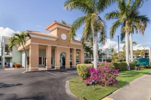 a building with palm trees and flowers in a parking lot at Quality Inn Boca Raton University Area in Boca Raton