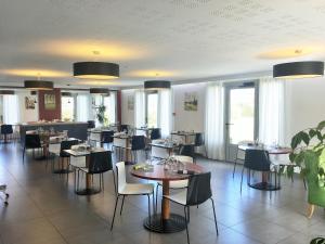 un comedor con mesas, sillas y ventanas en Brit Hotel Mayenne en Mayenne