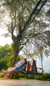 two women sitting on a swing in front of a tree at PARKROYAL Penang Resort in Batu Ferringhi
