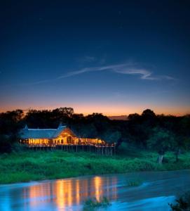 a house lit up at night next to a river at Lion Sands Narina Lodge in Sabi Sand Game Reserve