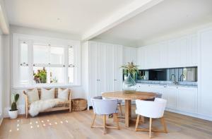 a white kitchen with a wooden table and white chairs at THE CAPE at Wategos - Lodging in Paradise in Byron Bay