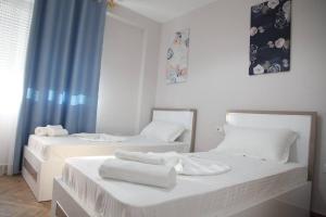 2 camas blancas en una habitación con cortinas azules en Shëngjini Apartments -Twin Towers-, en Shëngjin
