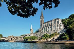 a large building with a steeple in front of a body of water at La Sainte Famille in Lourdes