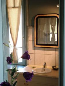 uma casa de banho com lavatório, espelho e flores roxas em Maison d'hôtes La Tuilerie em Peschadoires