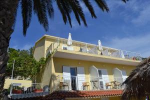 a yellow house with a balcony with chairs on it at Palma Promajna Apartments in Promajna