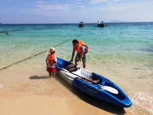 a man and a child standing next to a boat on the beach at Phi Phi Relax Beach Resort in Phi Phi Islands