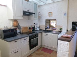 eine Küche mit weißen Schränken und einer Spüle und einer Mikrowelle in der Unterkunft Gîte de vacances avec wifi in Quistinic