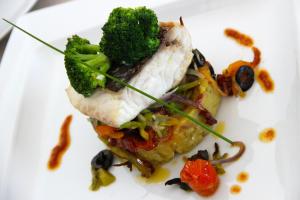 a white plate with a piece of fish and broccoli at Martinhal Sagres Beach Family Resort Hotel in Sagres