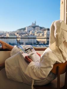 una persona sentada en una silla leyendo un libro en Hotel Belle-Vue Vieux-Port, en Marsella