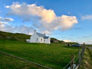 a white house on a green field with a fence at Harris White Cottage in Rodel